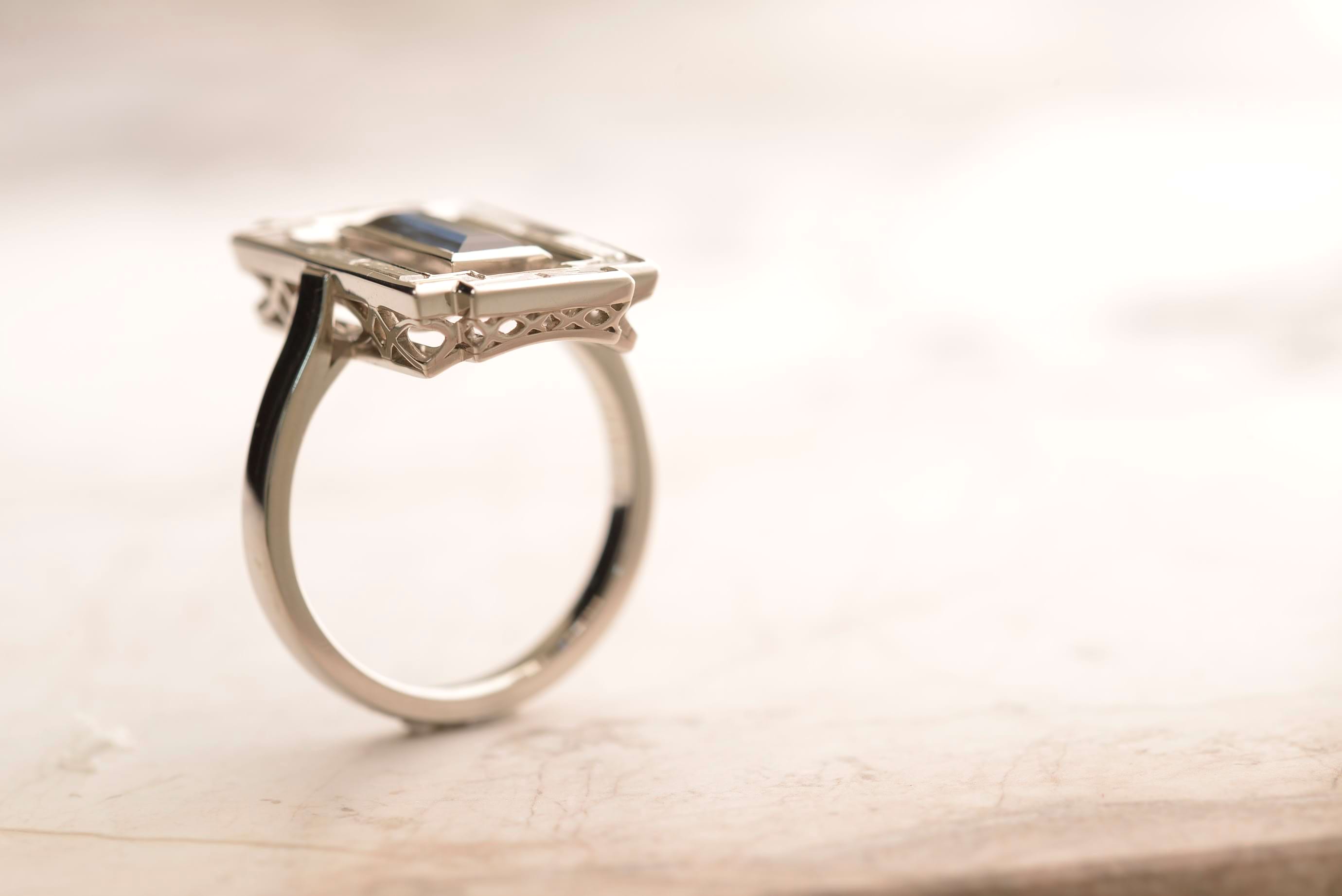 Side view of Art Deco-style platinum ring with a baguette-cut Australian sapphire centrepiece flanked by baguette-cut diamonds and arranged in a filigree basket. Handmade by Sydney jeweller Nicky Burles.