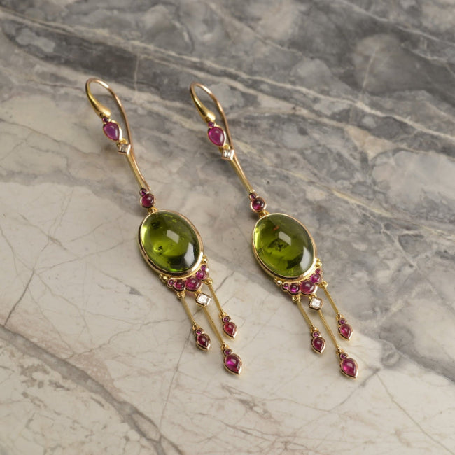 Bespoke tassel earrings featuring 24.6 ct oval peridots, adorned with cabochon rubies and diamond elements. Handmade in 18ct rose gold by Sydney jeweller Nicky Burles.