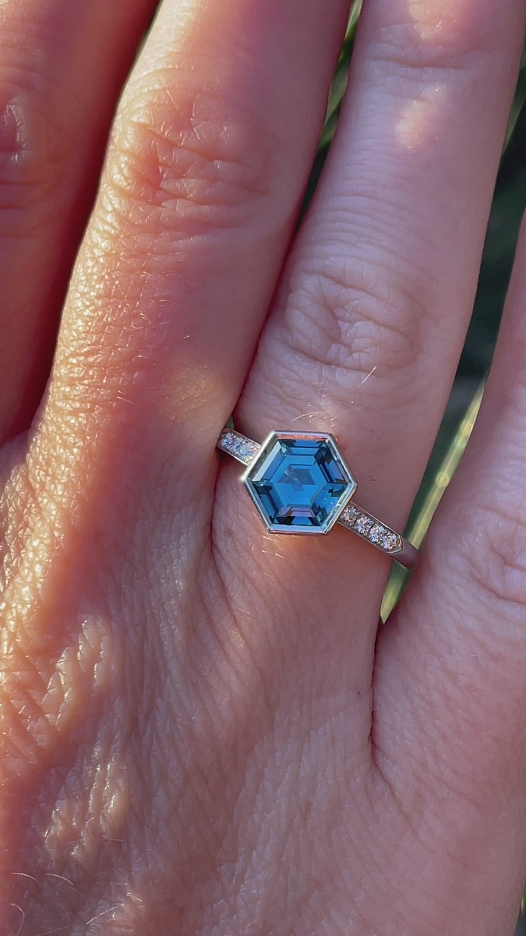 Platinum ring on hand featuring a hexagon-cut unheated teal sapphire from Madagascar, and 8 small diamonds in the shoulder. Handmade by Sydney jeweller Nicky Burles.