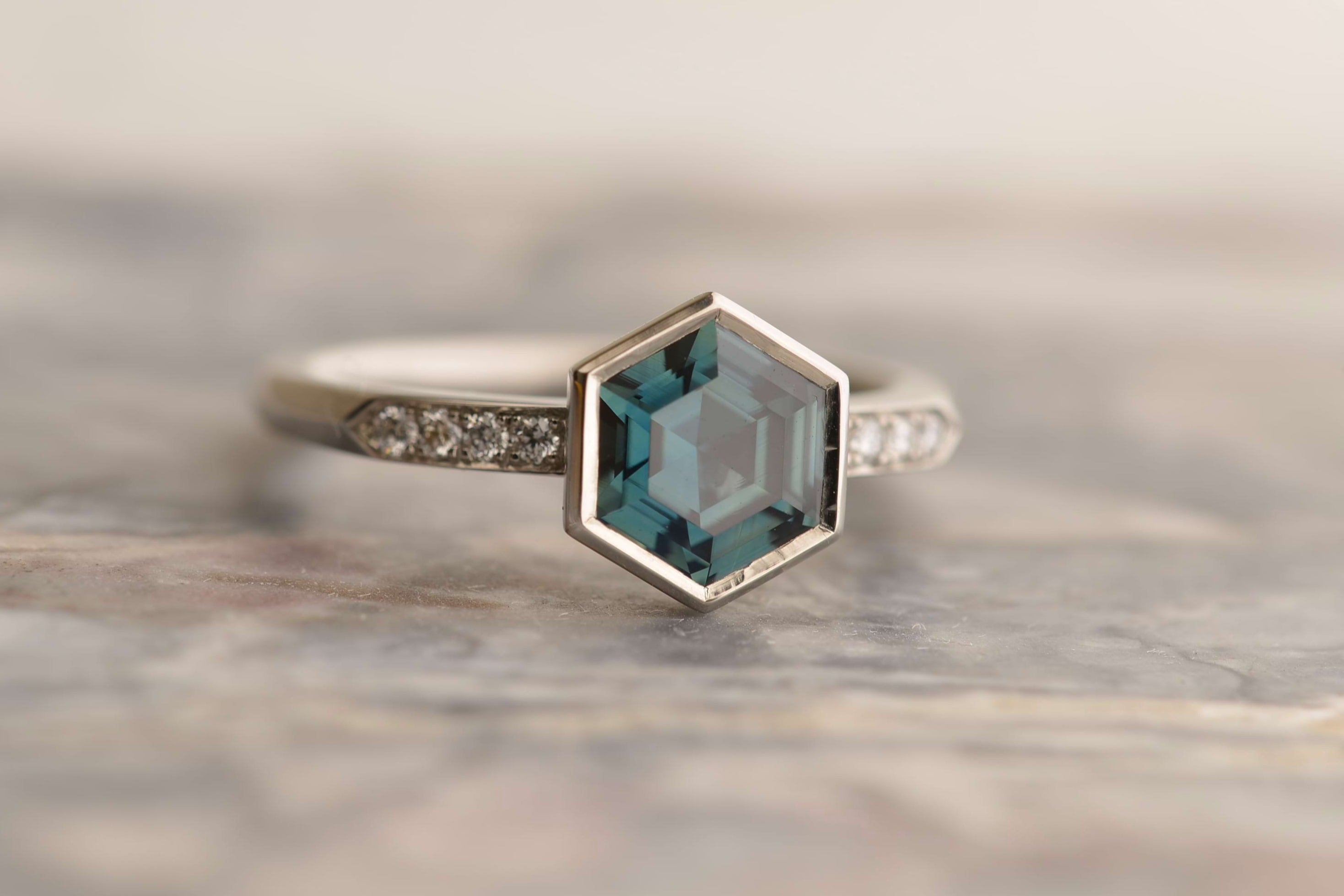 Platinum ring featuring a hexagon-cut unheated teal sapphire from Madagascar, and 8 small diamonds in the shoulder. Handmade by Sydney jeweller Nicky Burles.