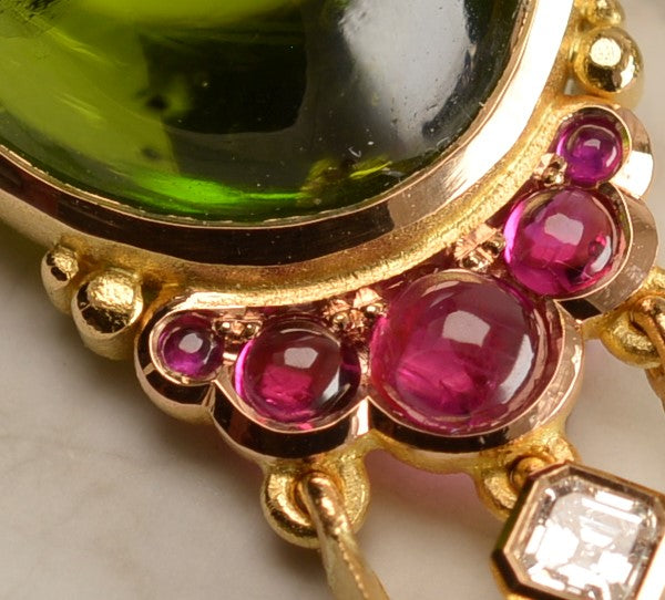 Close up of ruby cabochons set in 18ct rose gold on bespoke tassel earrings with oval peridot centre stones. Handmade by Sydney jeweller Nicky Burles.